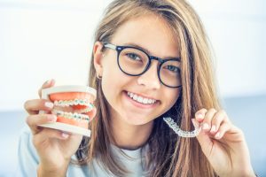 girl holding model of braces and clear aligner